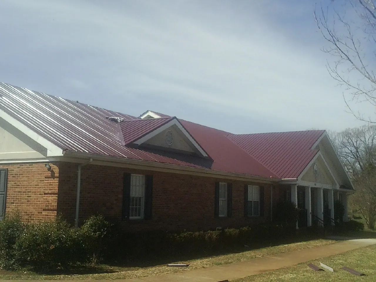Red metal roof with gabled entries on a long brick building, from a Hail Damage Roof Repair job in Rickman