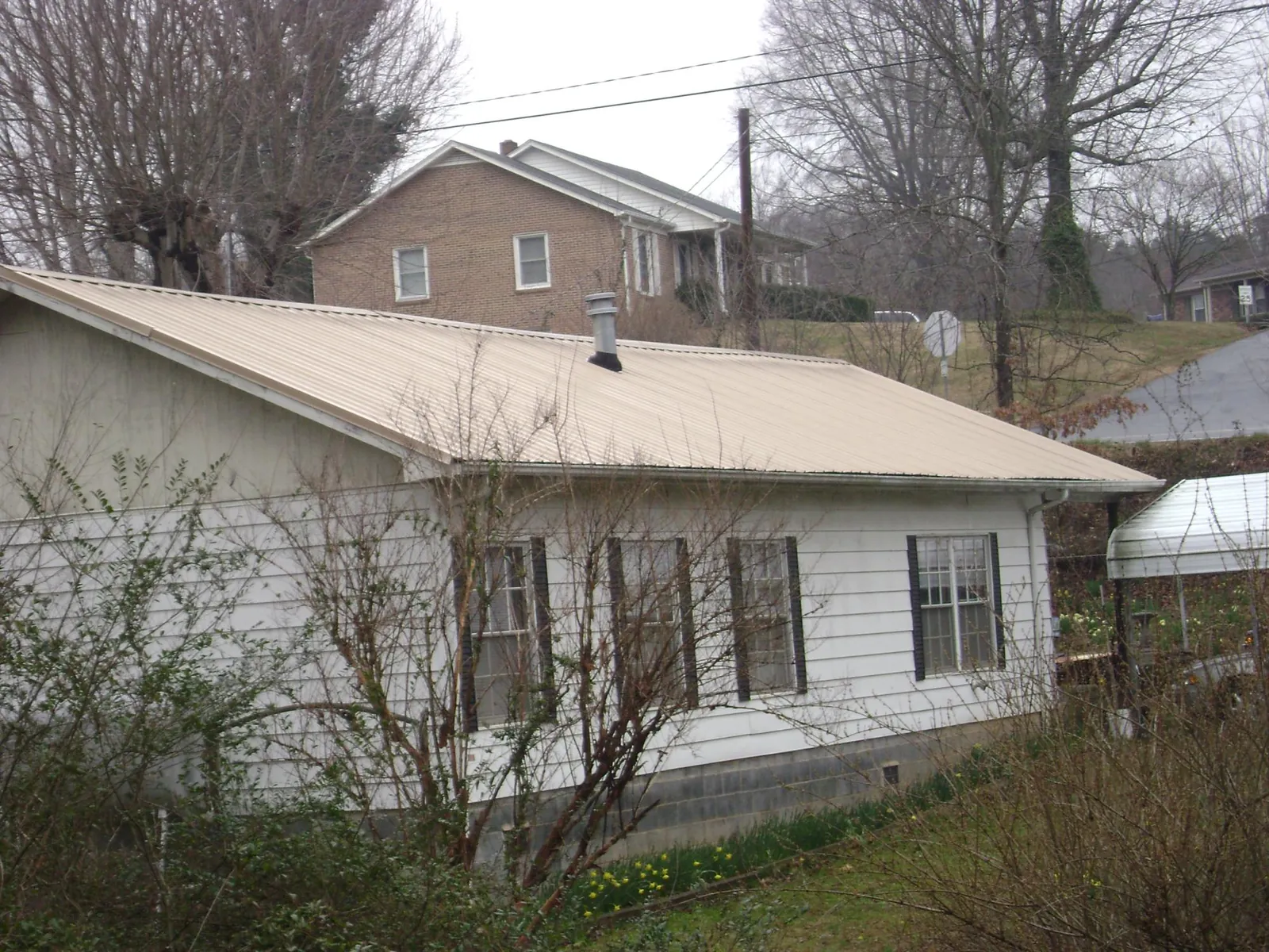 Tan metal roof on a white sided house set into a hillside — Commercial Roofing by Roofing Brothers in Rickman