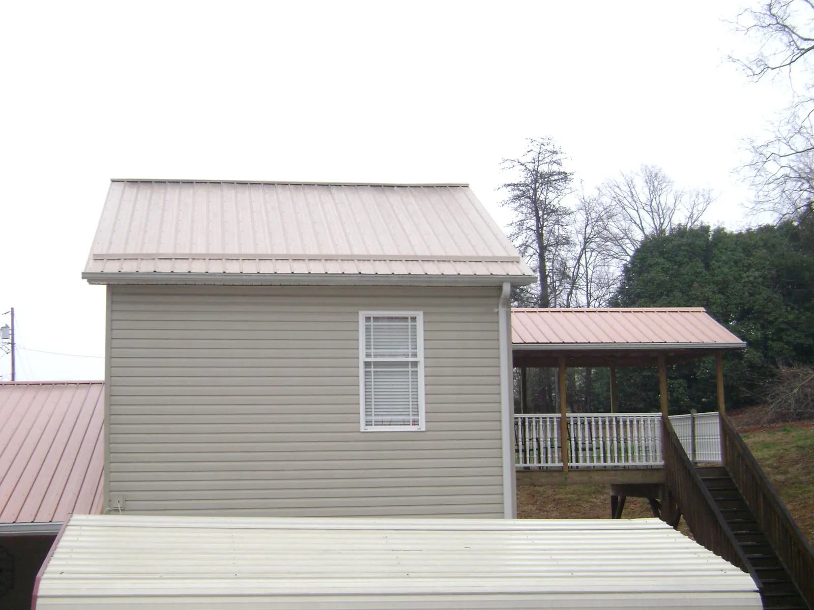Tan metal roofs on a two story addition and attached porch, from a Roof Replacement job in Rickman